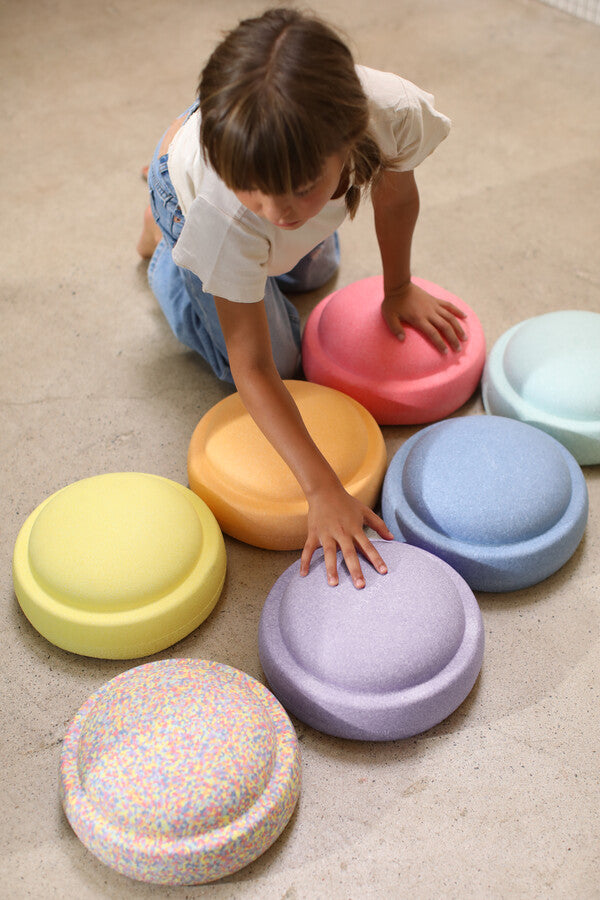 Kid is playing with Stapelstein Original rainbow pastel on the ground